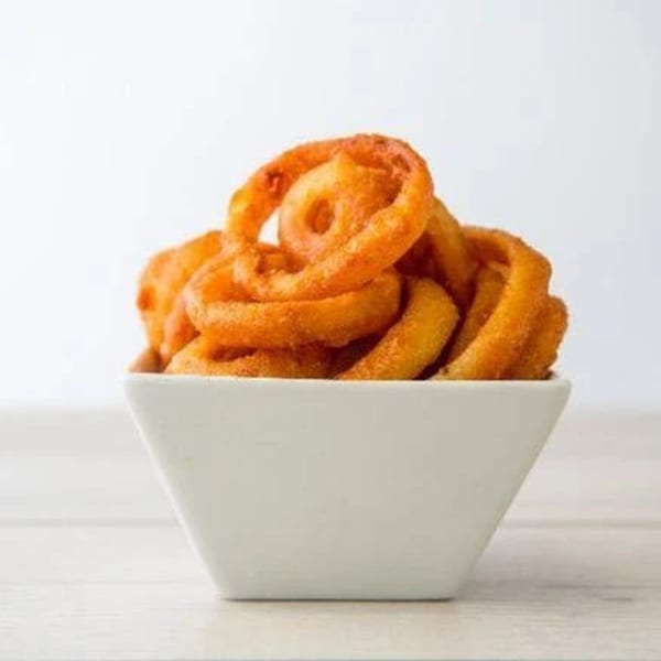 A white square bowl overflowing with golden-brown curly fries on a light wooden surface.