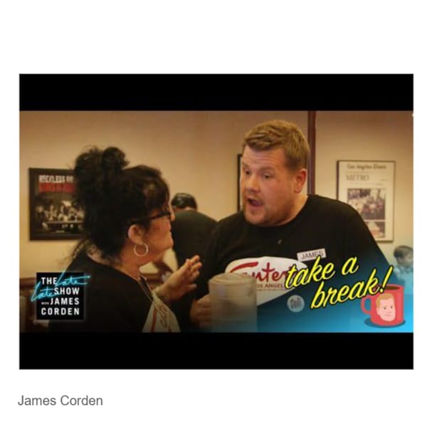 James Corden, wearing a Canter's Deli shirt, talking to a woman in a restaurant setting.