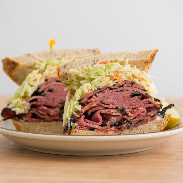 A Canter's Deli pastrami sandwich with coleslaw on rye bread, served with a pickle spear.