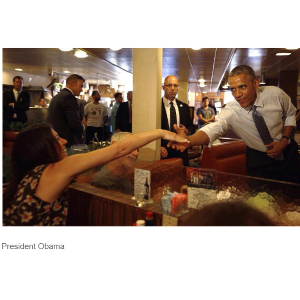 President Obama shaking hands with a woman across a counter at Canter's Deli.