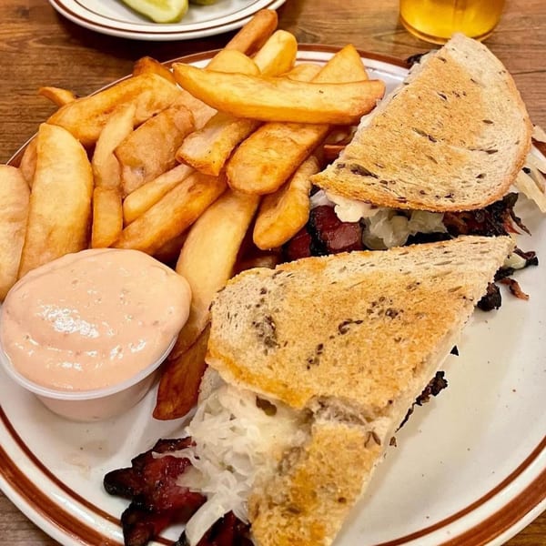 Canter's Deli pastrami sandwich with sauerkraut and fries, served with a side of Russian dressing.