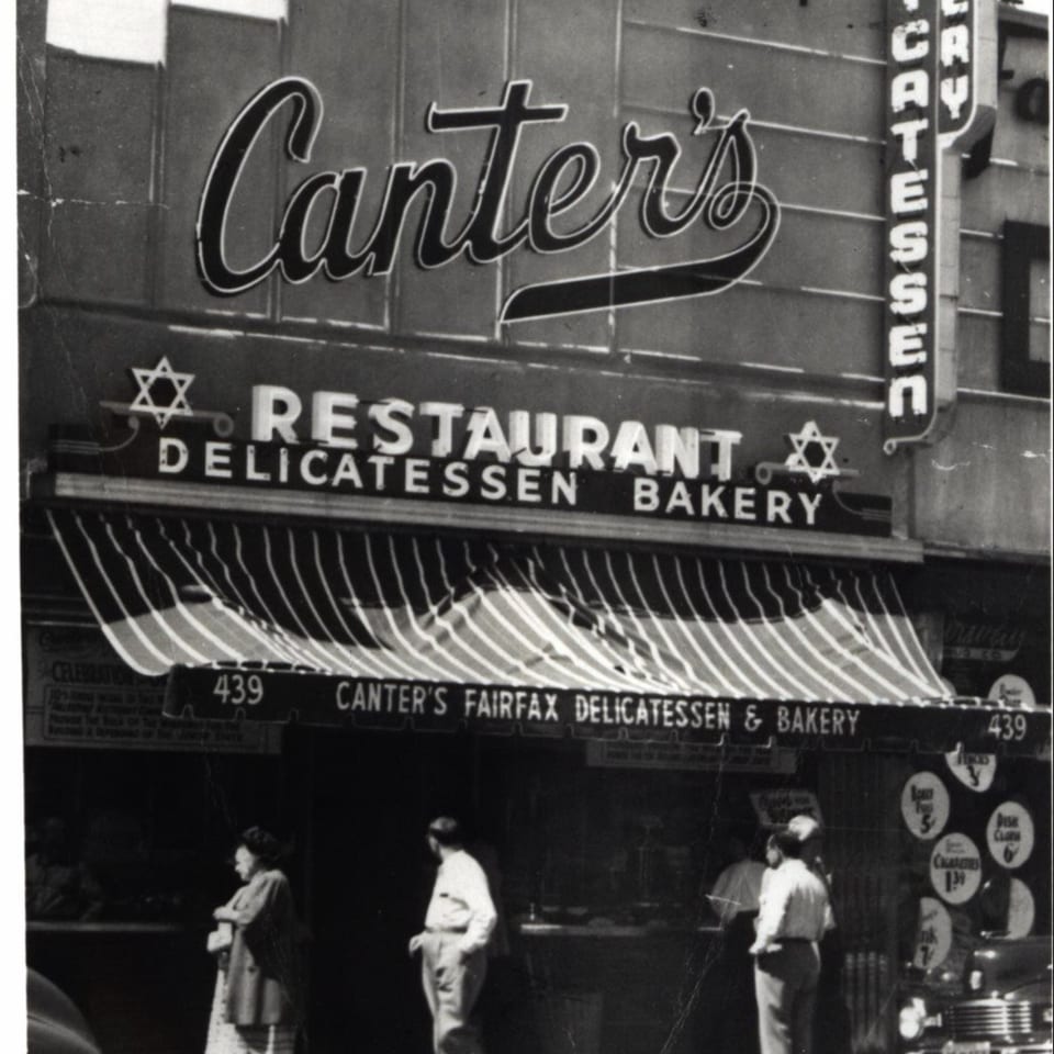 Black and white photo of Canter's Deli exterior with striped awning and people walking by.