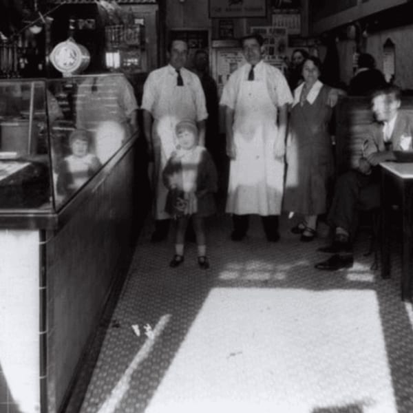 Black and white photo of a family, including two men in aprons, inside Canter's Deli.