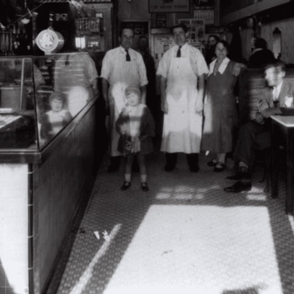 Black and white photo of a family, including two men in aprons, inside Canter's Deli.