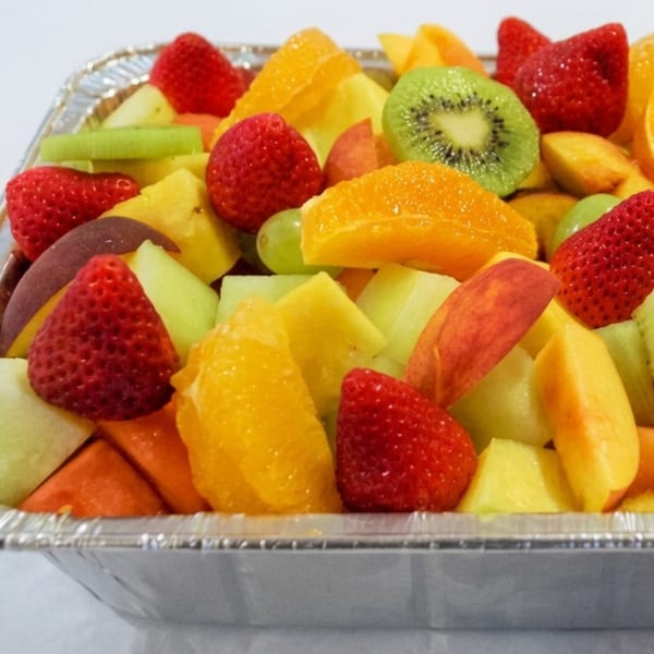 A large aluminum tray filled with a colorful assortment of fresh-cut fruit, including strawberries, kiwi, and oranges.