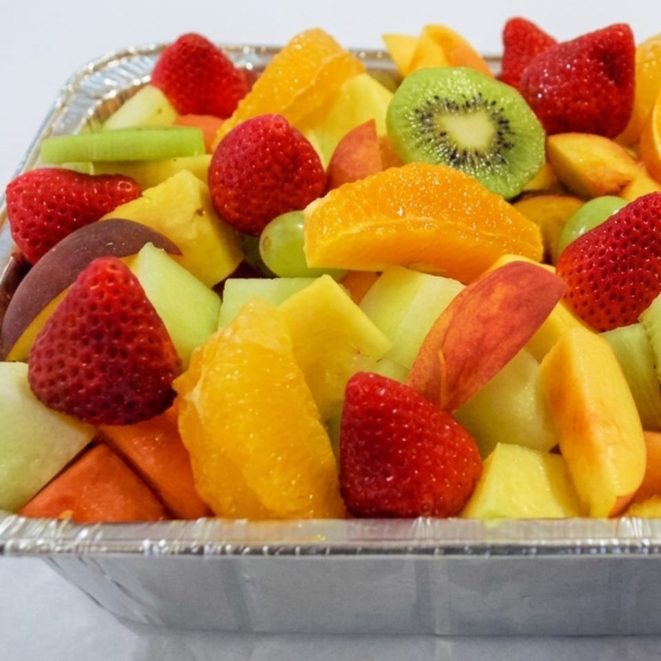 A large aluminum tray filled with a colorful assortment of fresh-cut fruit, including strawberries, kiwi, and oranges.