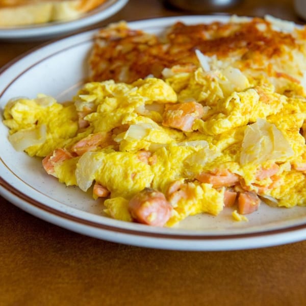 Scrambled eggs with lox and onions, served with crispy hash browns on a white plate.