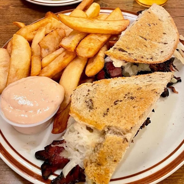 Canter's Deli pastrami sandwich with sauerkraut and a side of thick-cut fries and dipping sauce.