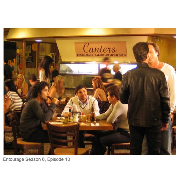 Diners seated at tables in Canter's Deli, with a deli counter and sign in the background.