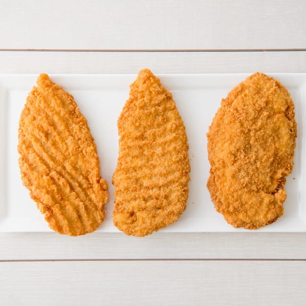 Three golden-brown fried chicken cutlets, likely schnitzel, on a white rectangular plate.