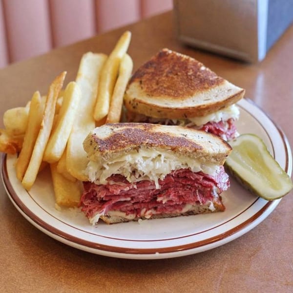Canter's Deli Reuben sandwich with corned beef, sauerkraut, and cheese, served with fries and a pickle.