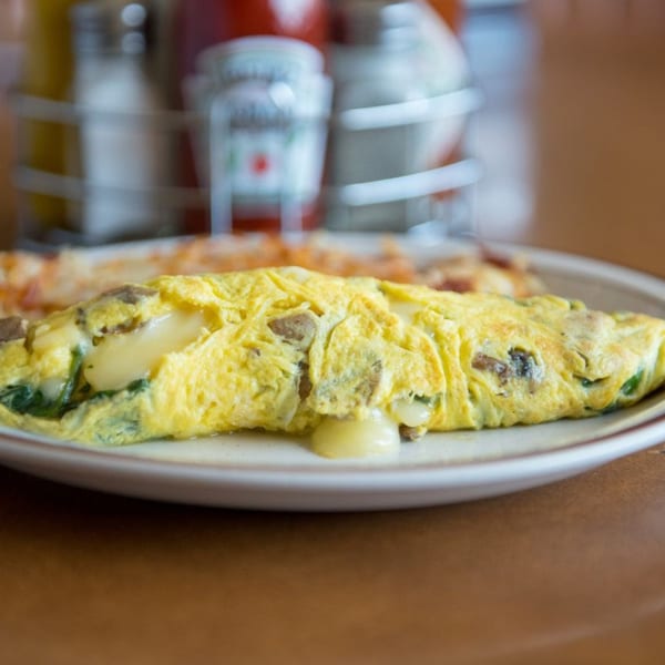 A golden omelet filled with melted cheese, spinach, and meat, served on a white plate.