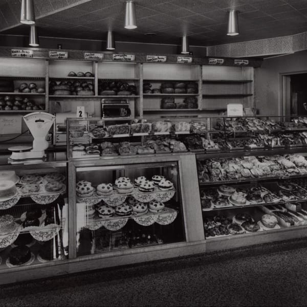 Black and white photo of a deli bakery display case filled with various breads, cakes, and pastries.