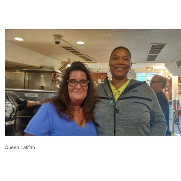 Queen Latifah smiling with another woman inside Canter's Deli, with kitchen equipment in the background.