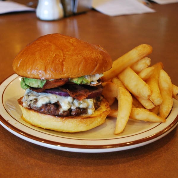 A Canter's Deli burger with avocado, bacon, red onion, and melted cheese, served with fries.