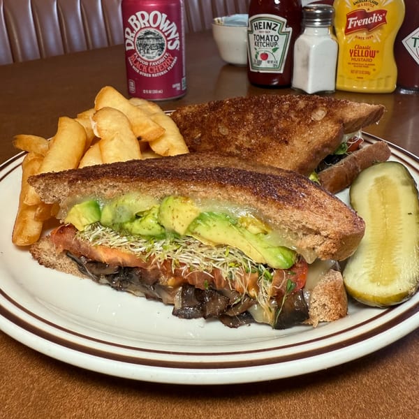 Canter's Deli grilled sandwich with avocado, sprouts, and mushrooms, served with fries, pickle, and soda.