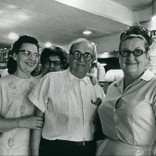 Four smiling people, two men and two women, pose together in a vintage deli setting.