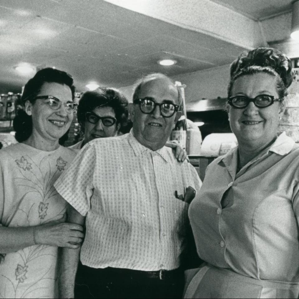 Four smiling people, two men and two women, pose together in a vintage deli setting.