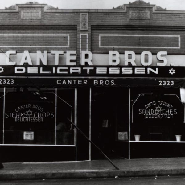 Black and white photo of the original Canter Bros. Delicatessen storefront with signs for steaks, chops, and sandwiches.
