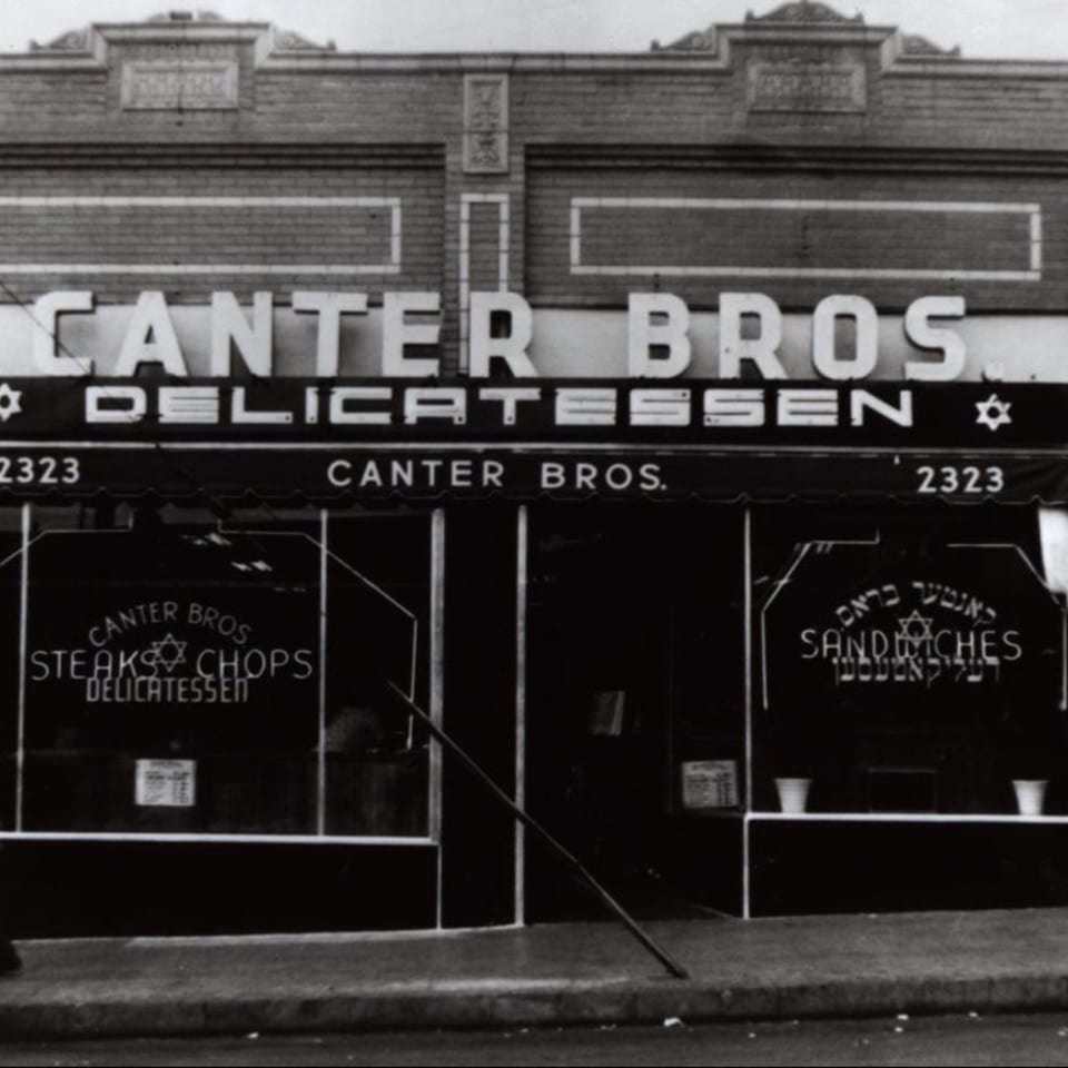 Black and white photo of the original Canter Bros. Delicatessen storefront with signs for steaks, chops, and sandwiches.